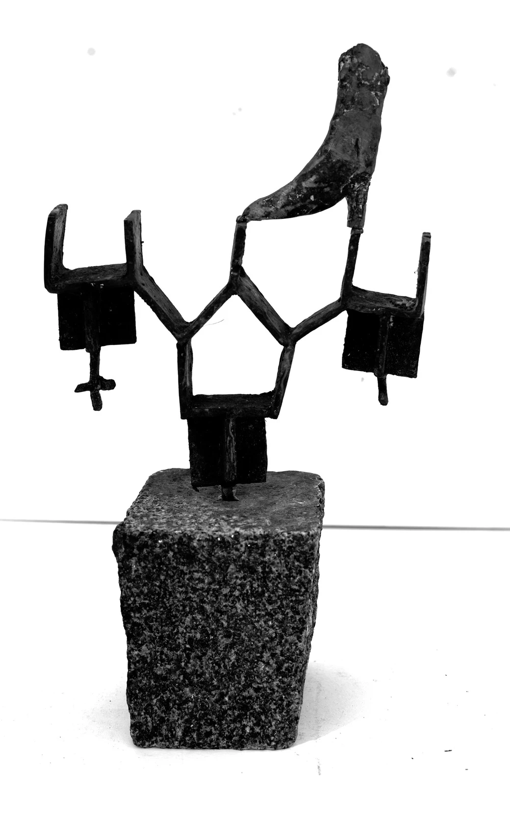 Sculpture in black metal on a granite base: a bird carrying a chair on its head.